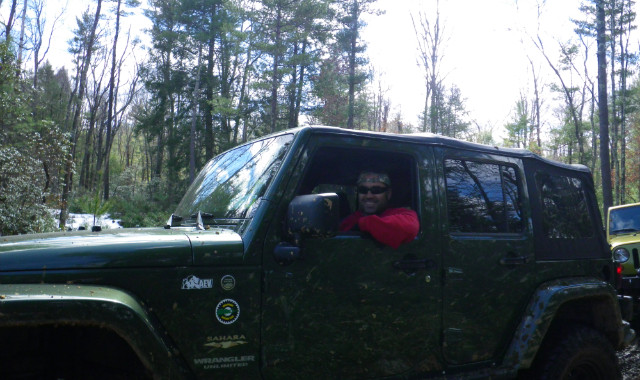 Man in red shirt driving green Jeep Wrangler