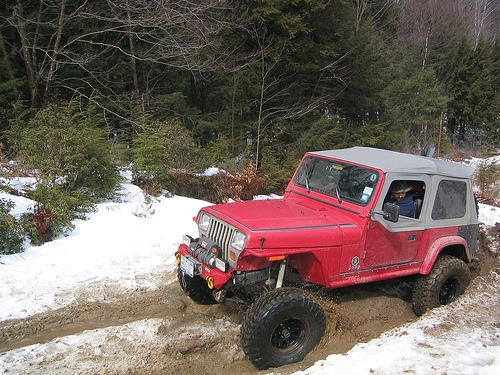 Red Jeep traversing snowy, muddy trail