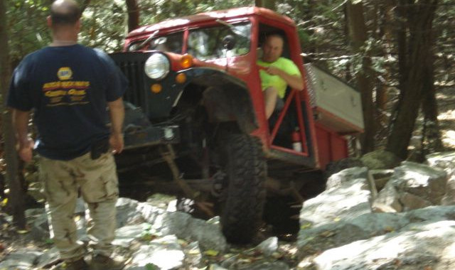 Man driving red Jeep over rocks