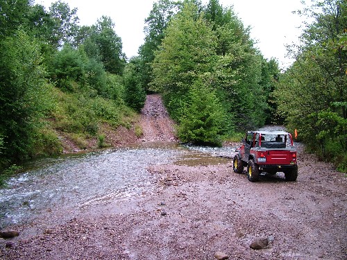 Red Jeep crossing shallow stream on off-road trail
