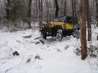 Yellow Jeep navigating snowy, rocky terrain