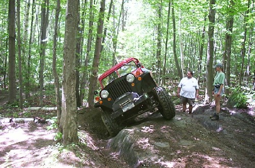 Red Jeep navigating rocky trail, two onlookers