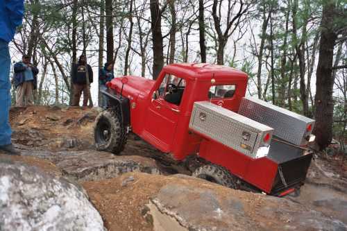 Red Jeep truck navigating rocky terrain