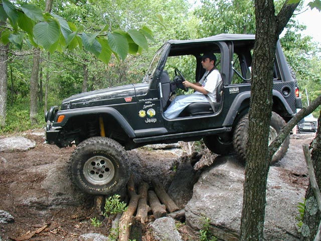 Man driving Jeep over rocks and logs