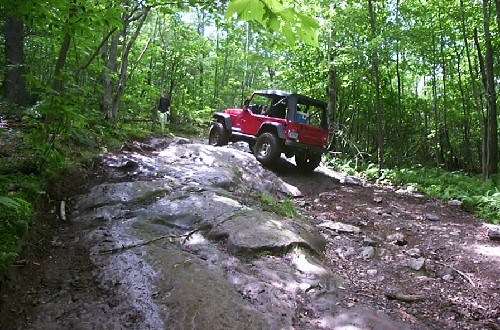 Red Jeep traversing rocky, muddy trail