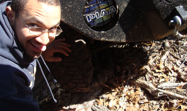Man playfully poses near muddy off-road tire