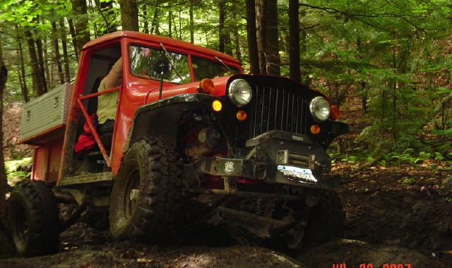 Red Jeep truck off-roading in woods
