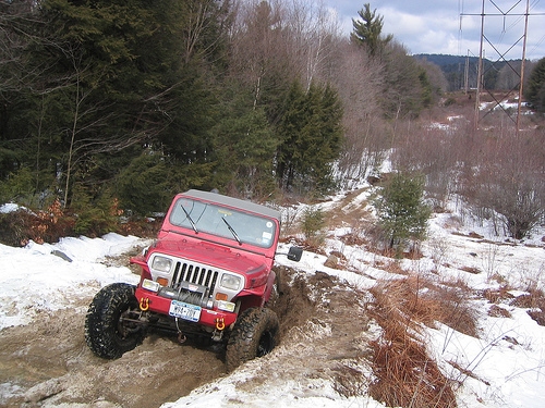 Red Jeep navigating snowy, muddy trail