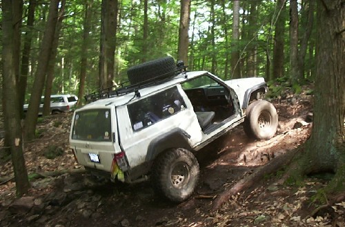 White Jeep Cherokee navigating a muddy forest trail