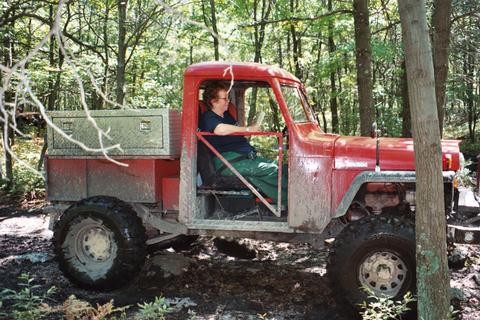 Person driving a muddy red truck on a trail