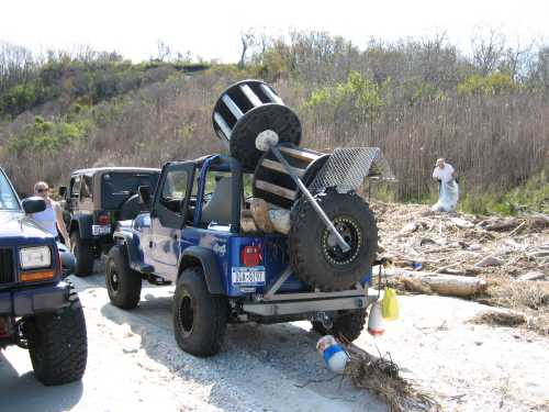 Blue Jeep with large spool on back, beach setting