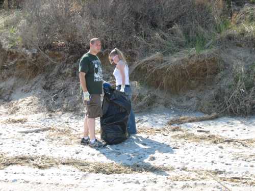 Couple collecting beach trash in a black bag