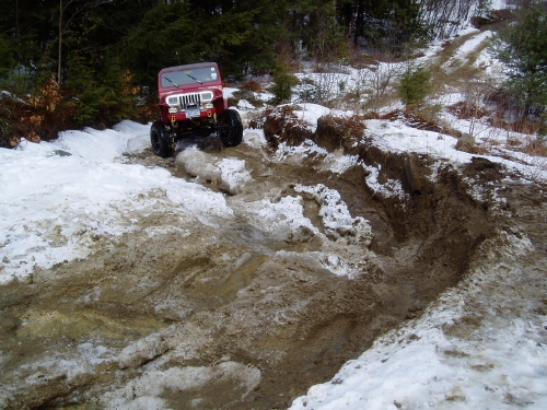 Red Jeep navigating snowy, muddy off-road trail