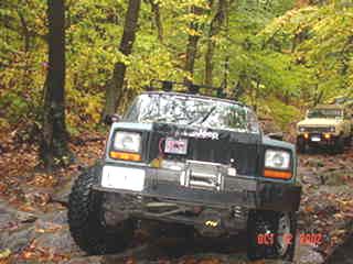 Green Jeep Cherokee off-roading in autumn woods