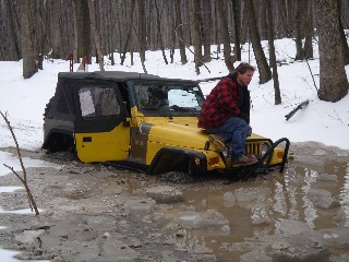 Man on stuck yellow Jeep in snowy woods