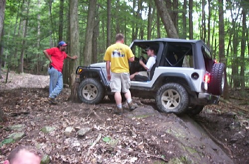 White Jeep navigating rocky trail, three men observing