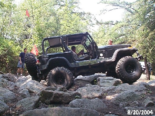 Black Jeep navigating rocky terrain; onlookers nearby