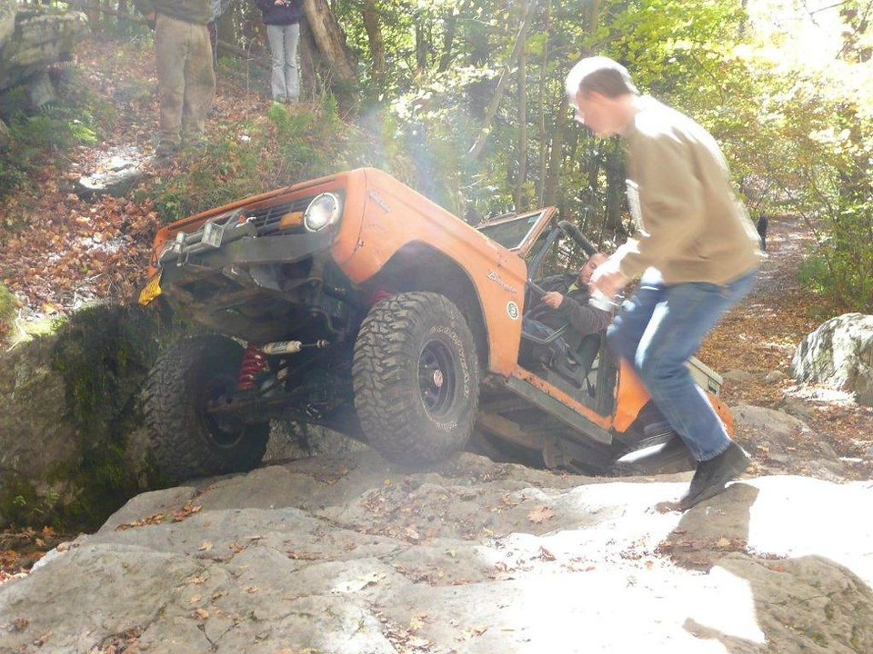 Man helps orange Ford Bronco climb rocks