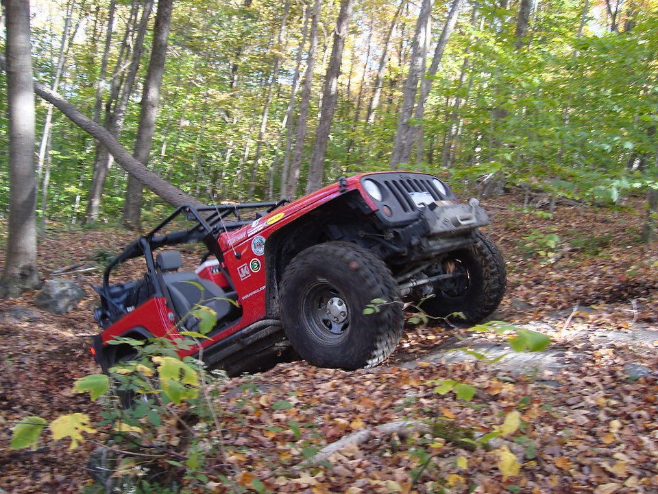 Red Jeep Wrangler off-roading in autumn woods