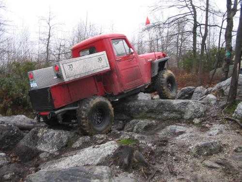 Red Jeep truck off-roading over rocks