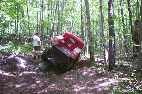 Red truck climbing rocky trail in woods