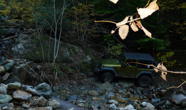 Jeep traversing rocky stream, autumn leaves