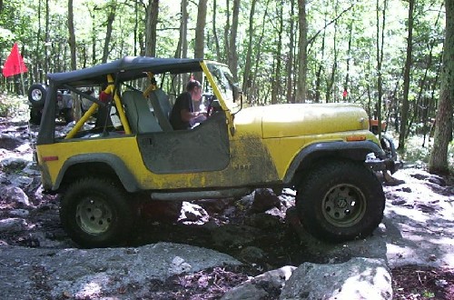 Person driving yellow Jeep on rocks