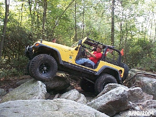 Man driving yellow Jeep over rocks
