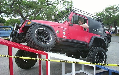 Man in red Jeep ascending ramp; Caution