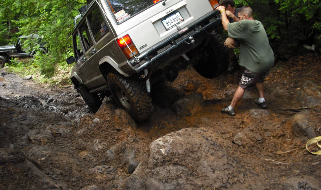 Men pushing Jeep Cherokee up muddy hill