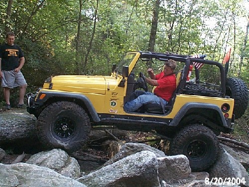 Man driving yellow Jeep over rocks