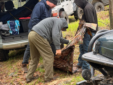 A bunch of men trying to figure out how to fold a toilet tent.