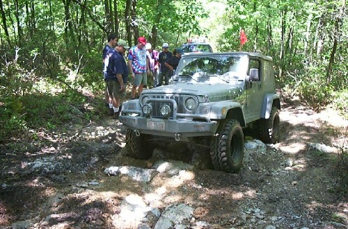 Jeep navigating rocky trail, onlookers present