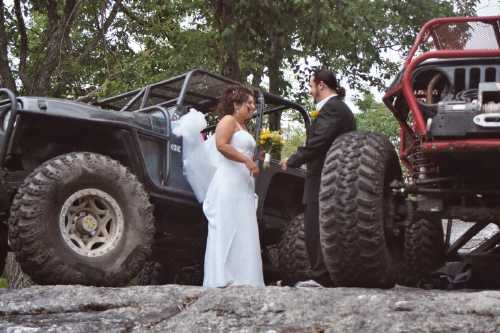 Bride and groom pose by off-road vehicles