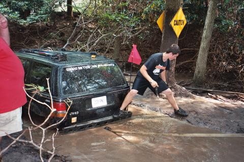 Man pushing stuck Jeep, Caution sign visible, mud
