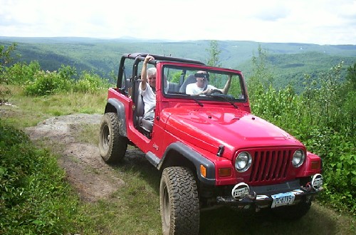 Red Jeep on trail, two people enjoying scenic view