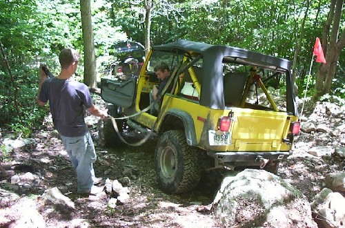 Two men assisting yellow Jeep on rocky trail
