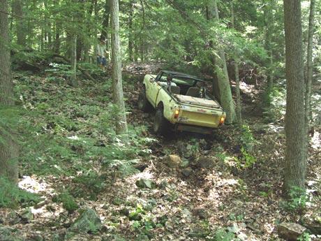 Yellow Jeep traversing a wooded, rocky trail