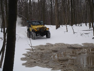 Yellow Jeep traversing snowy, muddy trail