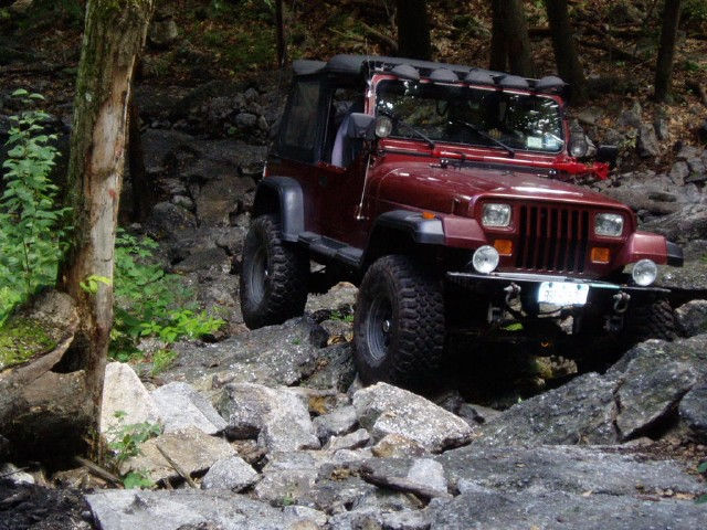 Red Jeep Wrangler traversing rocky terrain