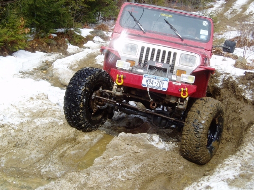 Red Jeep Wrangler navigating snowy, muddy trail