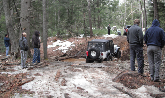 Jeep stuck in muddy trail, onlookers watching