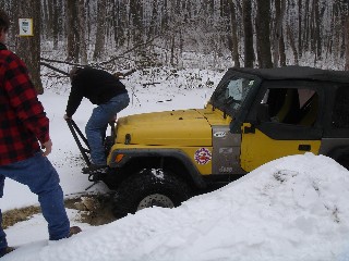 Man pushing yellow Jeep stuck in snowy woods