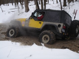 Yellow Jeep traversing snowy, muddy terrain