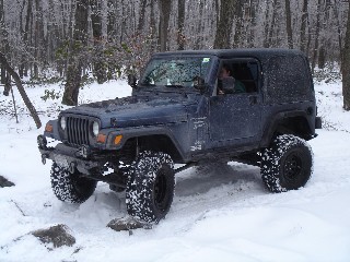 Man driving dark-blue Jeep Wrangler in snowy woods