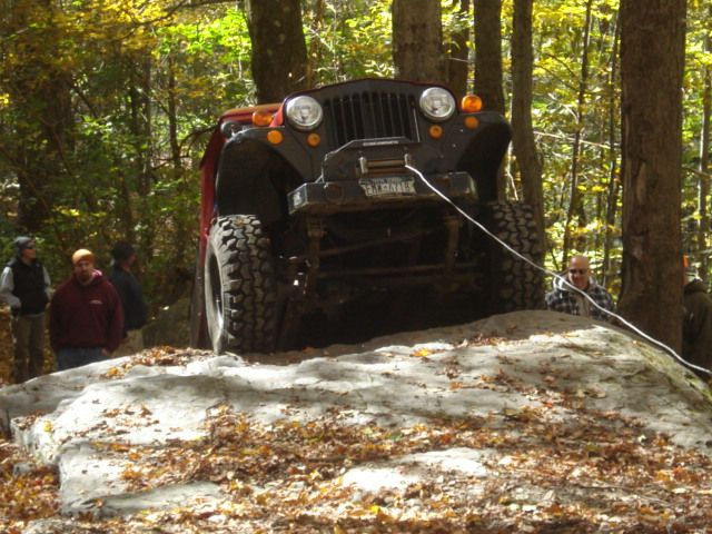 Red Jeep tackling rocky terrain, autumn leaves
