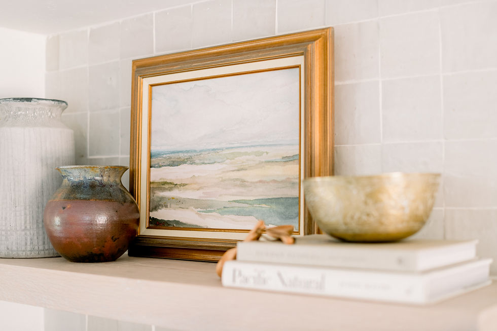 Coastal painting in gold vintage frame sitting atop a white wood shelf in kitchen