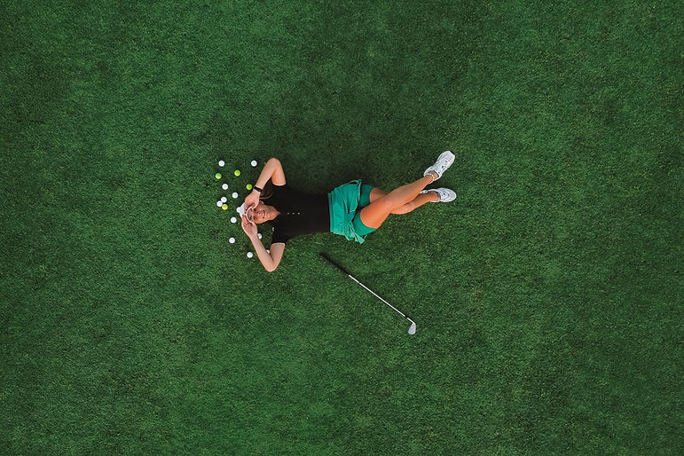 Aerial view of a young attractive woman in sportswear and a cap, who is lying on the green