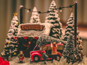 Miniature Christmas village scene with a red car and family bringing home a tree, symbolizing slowing down and recalibrating the holidays.