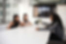 Three women in a meeting, discussing a job interview at a table.